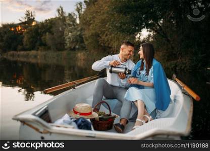 Love couple with thermos in a boat on quiet lake at sunset. Romantic meeting, boating trip, man and woman walking along the river. Love couple with thermos in a boat on quiet lake