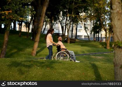 Love couple with wheelchair walking in autumn park. Paralyzed people and disability, care for a disabled woman. Smiling husband and wife overcome difficulties together, warm relationships. Love couple with wheelchair walking in autumn park