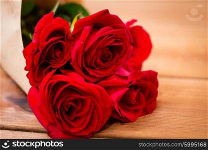 love, date, flowers, valentines day and holidays concept - close up of red roses bunch wrapped into brown paper on wooden table