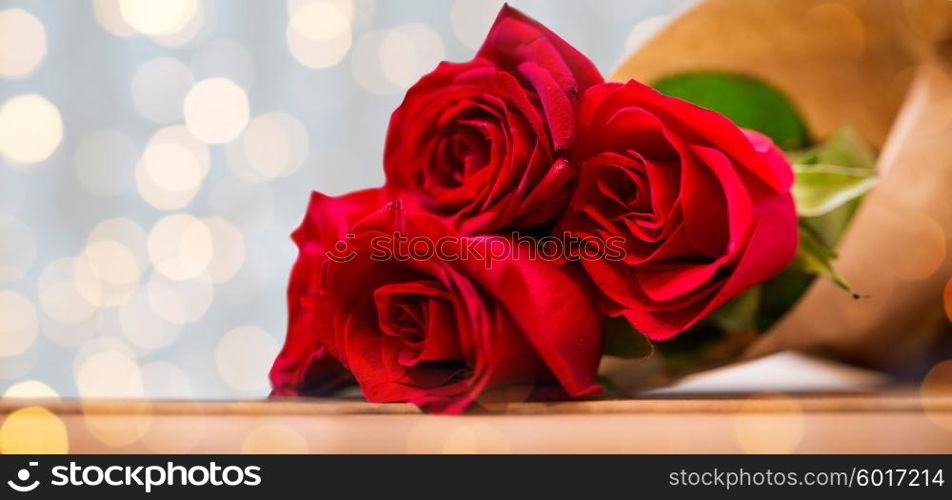 love, date, flowers, valentines day and holidays concept - close up of red roses bunch wrapped into brown paper on wooden table over golden lights