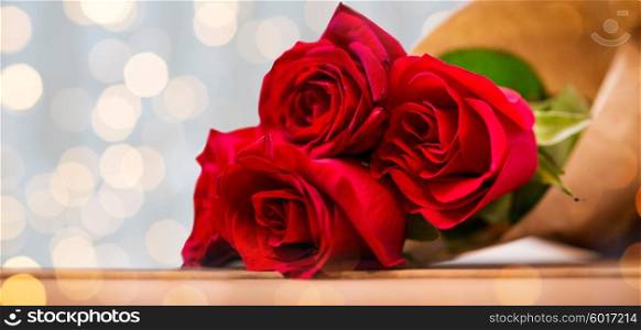 love, date, flowers, valentines day and holidays concept - close up of red roses bunch wrapped into brown paper on wooden table over golden lights