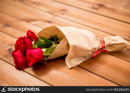 love, date, flowers, valentines day and holidays concept - close up of red roses bunch wrapped into brown paper on wooden table