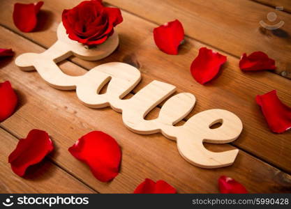 love, date, romance, valentines day and holidays concept - close up of word love cutout with red rose petals on wood