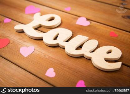 love, date, romance, valentines day and holidays concept - close up of word love with red and pink paper hearts on wood