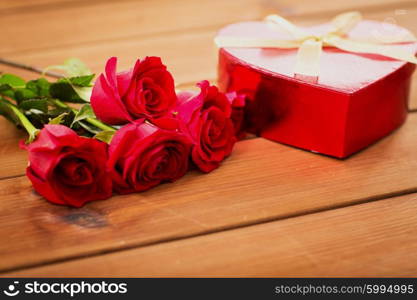 love, date, romance, valentines day and holidays concept - close up of heart shaped gift box and red roses on wooden table