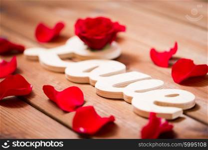 love, date, romance, valentines day and holidays concept - close up of word love cutout with red rose petals on wood