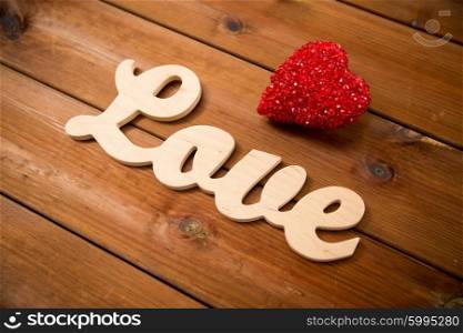 love, date, romance, valentines day and holidays concept - close up of word love with red heart decoration on wood