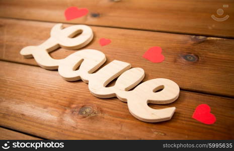 love, date, romance, valentines day and holidays concept - close up of word love with red paper hearts on wood