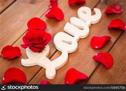 love, date, romance, valentines day and holidays concept - close up of word love cutout with red rose petals on wood
