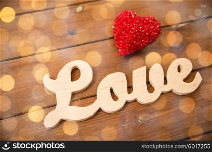 love, date, romance, valentines day and holidays concept - close up of word love with red heart decoration on wood over golden lights