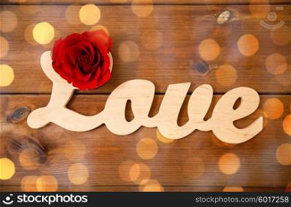 love, date, romance, valentines day and holidays concept - close up of word love cutout with red rose on wood over golden lights
