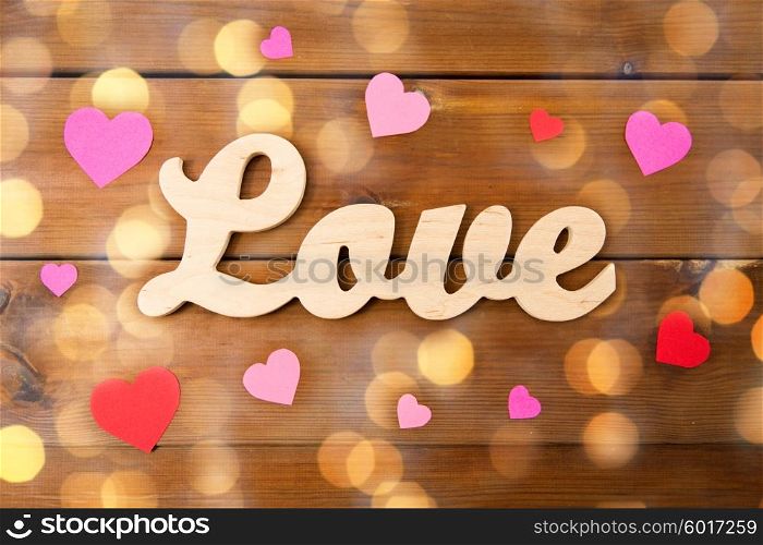 love, date, romance, valentines day and holidays concept - close up of word love with red and pink paper hearts and golden lights on wood