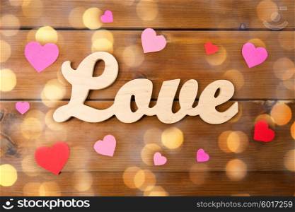 love, date, romance, valentines day and holidays concept - close up of word love with red and pink paper hearts and golden lights on wood