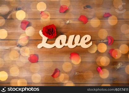 love, date, romance, valentines day and holidays concept - close up of word love cutout with red rose petals on wood over golden lights