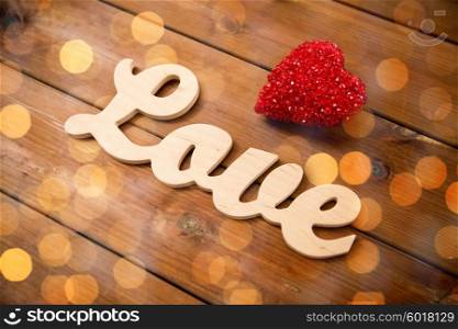 love, date, romance, valentines day and holidays concept - close up of word love with red heart decoration on wood