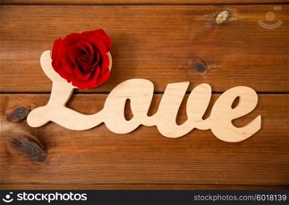 love, date, romance, valentines day and holidays concept - close up of word love cutout with red rose on wood