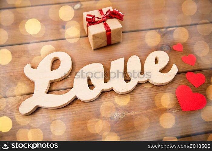 love, date, romance, valentines day and holidays concept - close up of word love with gift box and red hearts on wood