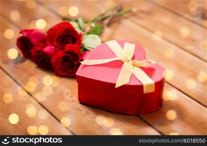 love, date, romance, valentines day and holidays concept - close up of heart shaped gift box and red roses on wooden table over lights background