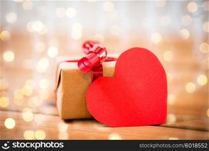 love, date, romance, valentines day and holidays concept - close up of gift box and blank red heart-shaped note on wood over lights background