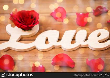 love, date, romance, valentines day and holidays concept - close up of word love cutout with red rose petals on wood over lights background