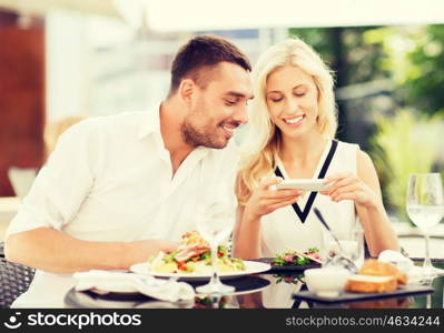 love, date, technology, people and relations concept - happy couple with smatphone taking picture of food at restaurant