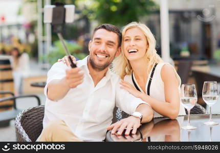 love, date, technology, people and relations concept - happy happy couple taking picture with smartphone on selfie stick at city street cafe or restaurant