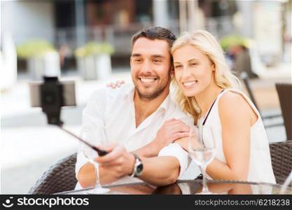 love, date, technology, people and relations concept - happy happy couple taking picture with smartphone on selfie stick at city street cafe or restaurant