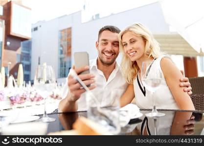 love, date, technology, people and relations concept - smiling happy couple taking selfie with smatphone at restaurant terrace