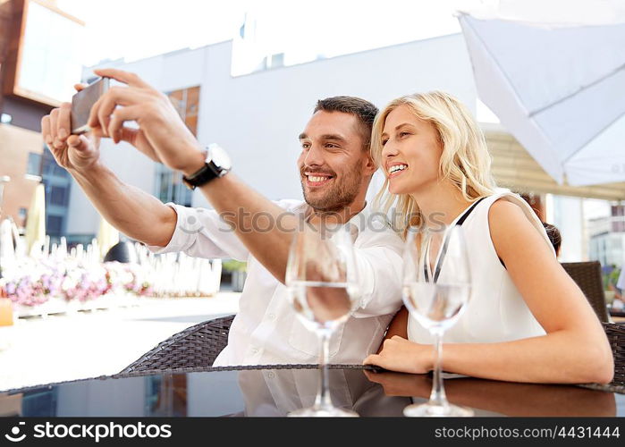 love, date, technology, people and relations concept - smiling happy couple taking selfie with smatphone at restaurant terrace