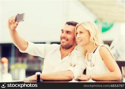 love, date, technology, people and relations concept - smiling happy couple taking selfie with smartphone at city street cafe
