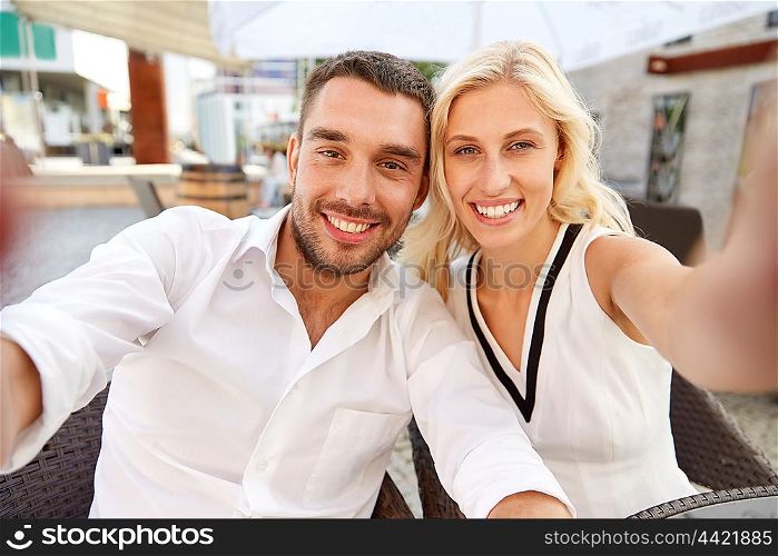 love, date, technology, people and relations concept - smiling happy couple taking selfie at restaurant terrace