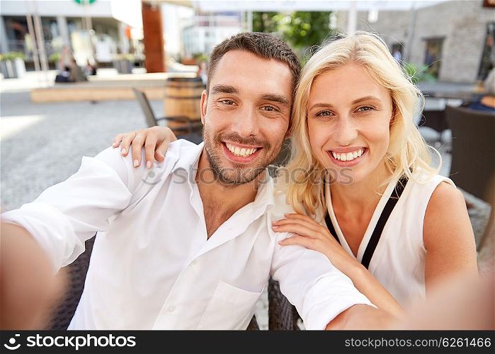 love, date, technology, people and relations concept - smiling happy couple taking selfie at restaurant terrace