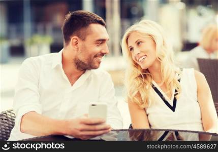 love, date, technology, people and relations concept - smiling happy couple with smatphone at city street cafe