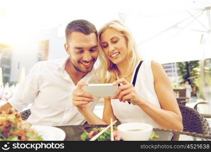love, date, technology, people and relations concept - smiling happy couple with smatphone at restaurant terrace