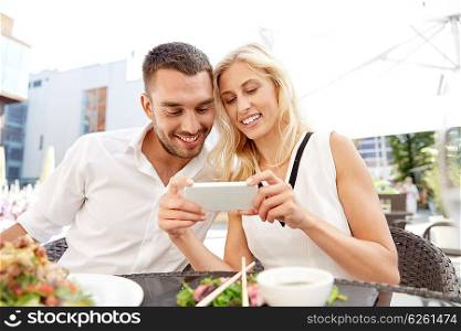 love, date, technology, people and relations concept - smiling happy couple with smatphone at restaurant terrace