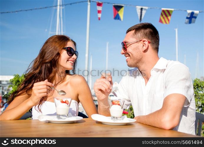 love, dating, people and food concept - smiling couple wearing sunglasses eating dessert and looking to each other at cafe