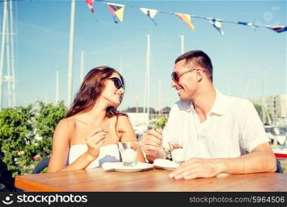 love, dating, people and food concept - smiling couple wearing sunglasses eating dessert and looking to each other at cafe
