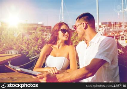 love, dating, people and food concept - smiling couple wearing sunglasses looking at each other and holding menu on cafe terrace