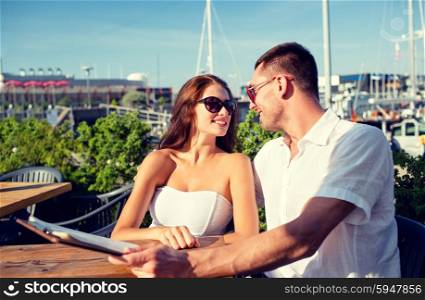 love, dating, people and food concept - smiling couple wearing sunglasses looking at each other and holding menu on cafe terrace