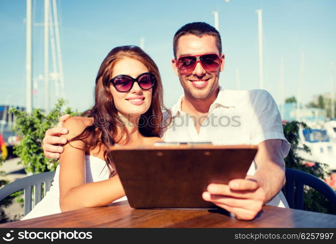 love, dating, people and food concept - smiling couple wearing sunglasses looking at menu on cafe terrace