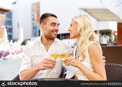 love, dating, people and holidays concept - happy couple drinking wine at open-air restaurant and clinking glasses