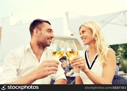 love, dating, people and holidays concept - happy couple drinking wine at open-air restaurant and clinking glasses