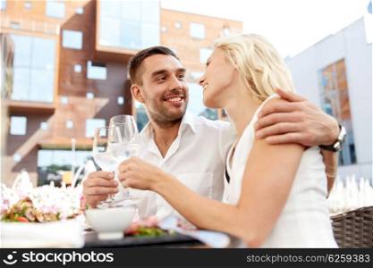 love, dating, people and holidays concept - happy couple drinking wine or water at open-air restaurant and clinking glasses