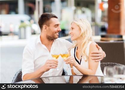 love, dating, people and holidays concept - smiling couple clinking glasses and looking to each other at restaurant lounge or terrace