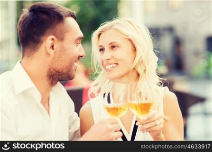 love, dating, people and holidays concept - smiling couple clinking glasses of wine and looking to each other at restaurant lounge or terrace