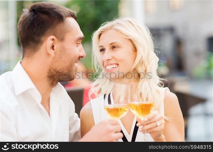 love, dating, people and holidays concept - smiling couple clinking glasses of wine and looking to each other at restaurant lounge or terrace