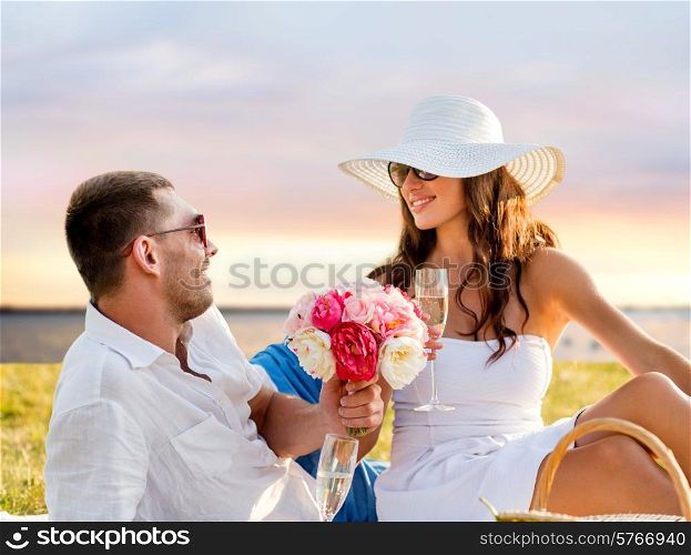 love, dating, people and holidays concept - smiling couple drinking champagne on picnic over seaside sunset background