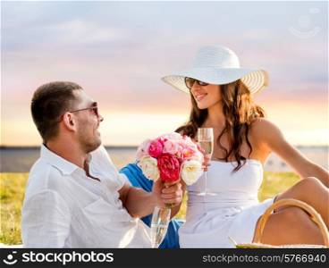 love, dating, people and holidays concept - smiling couple drinking champagne on picnic over seaside sunset background