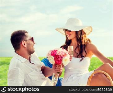 love, dating, people and holidays concept - smiling couple drinking champagne on picnic over blue sky and grass background