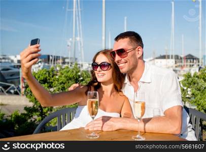 love, dating, people and holidays concept - smiling couple wearing sunglasses drinking champagne and making selfie at cafe